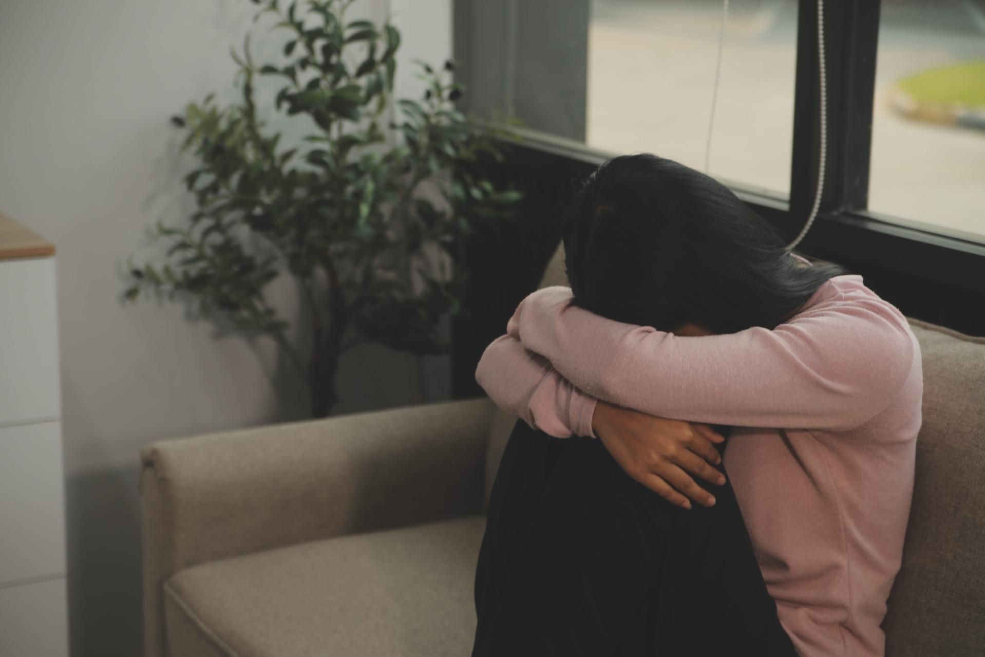 Una persona con un suéter rosa está sentada acurrucada en un sofá