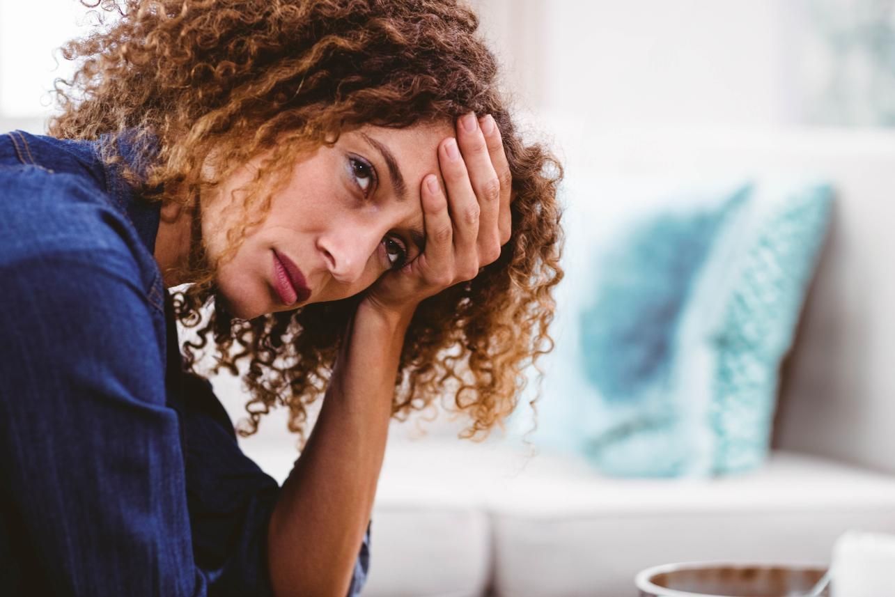Una persona con cabello rizado apoya la frente en la mano