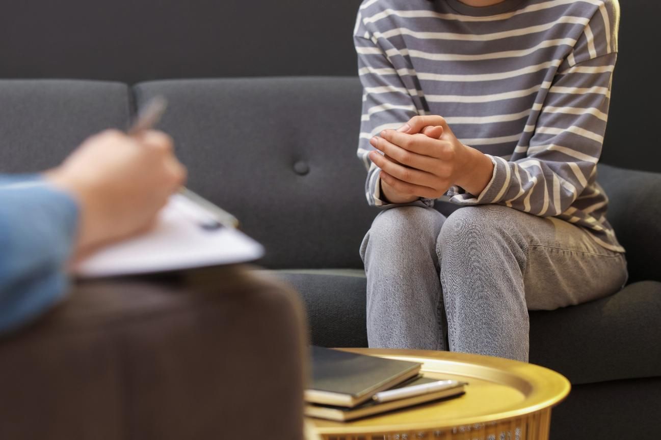 Un terapeuta sentado frente a un paciente en un sofá, tomando notas durante una consulta en un consultorio.