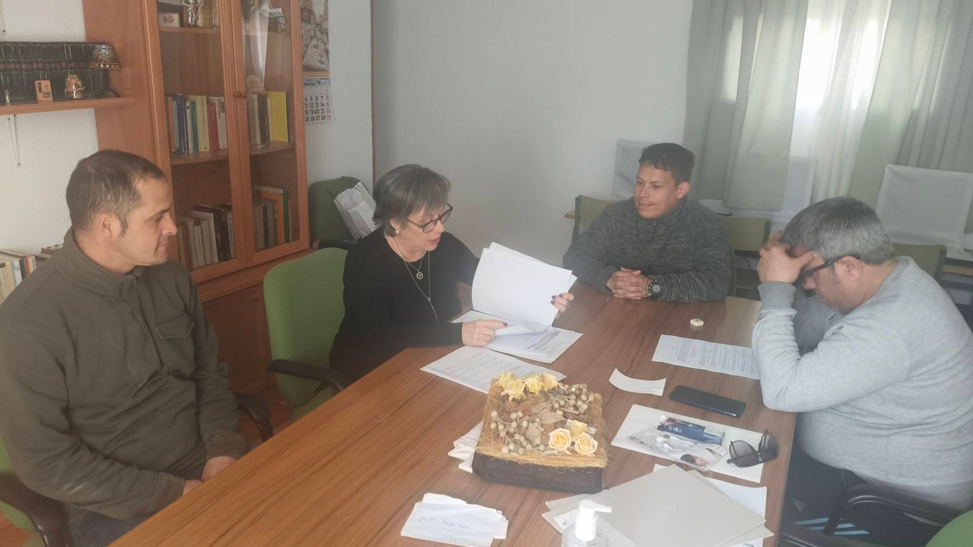 Cuatro personas están sentadas alrededor de una mesa de madera en una oficina, revisando documentos juntas.