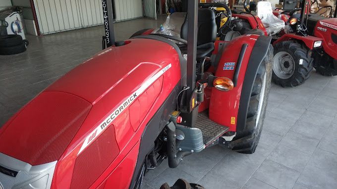 Un tractor rojo está estacionado en un garaje junto a otros tractores.