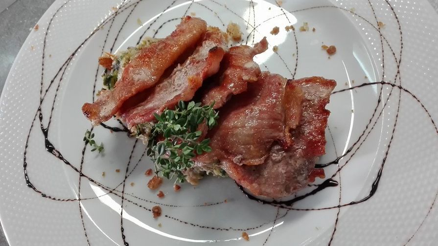 Prato gourmet com bacon, ervas e molho servido em um prato branco.