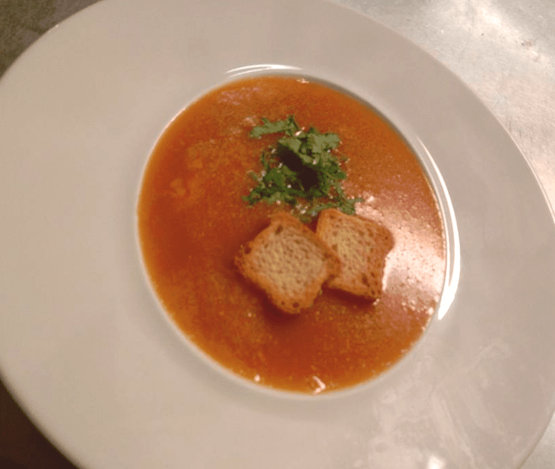 Sopa de tomate com croutons e salsa para decorar, servida em uma tigela branca.