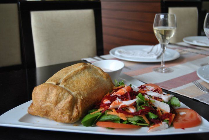 Um prato com um pastel grande, salada e molho para mergulhar; um copo de vinho sobre a mesa posta.