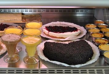 Exposição de sobremesas: Diversos bolos, cremes e parfaits em uma vitrine de vidro.