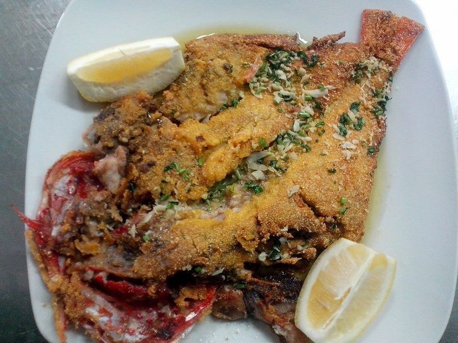 Peixe empanado com fatias de limão em um prato branco.