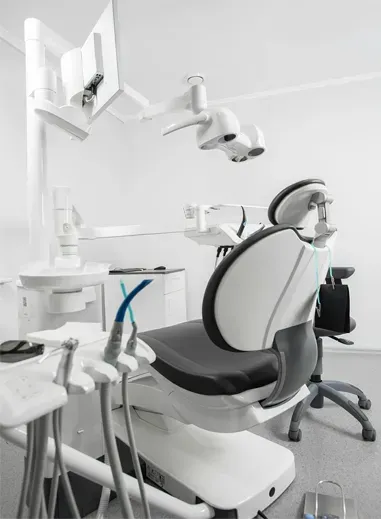 Cadeira odontológica em uma sala limpa e iluminada, com iluminação indireta e instrumentos acoplados.