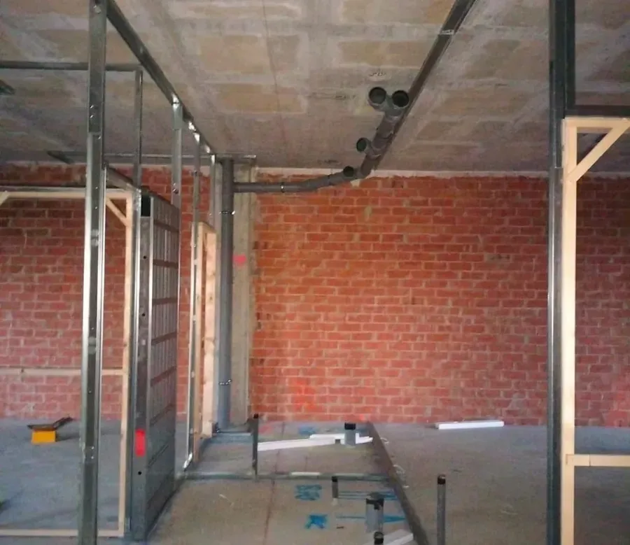 Obra en construcción con paredes de ladrillo visto, estructura metálica para tabiques y tuberías.