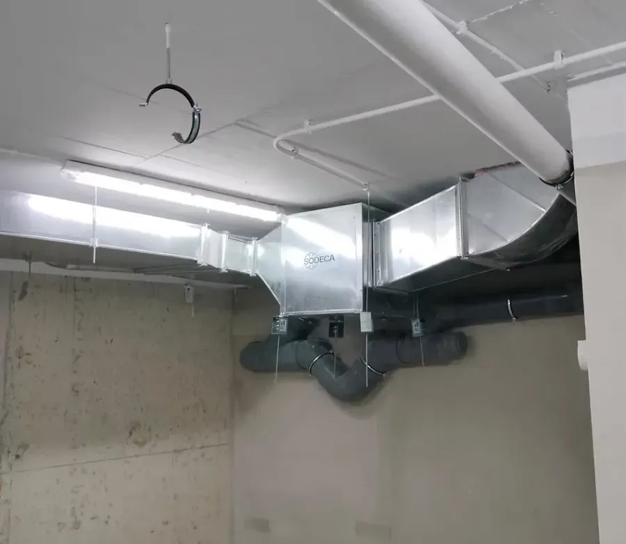 Instalación de techo industrial con conductos de aire rectangulares y tuberías de drenaje grises sobre un techo de hormigón.