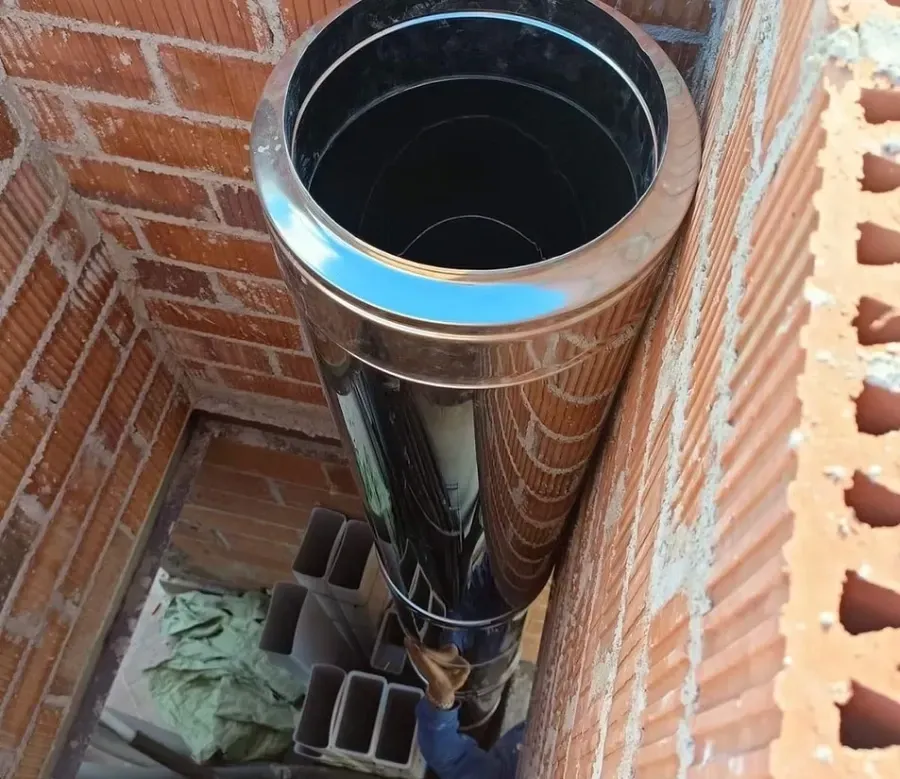Instalación de un tubo metálico de doble pared en posición vertical dentro de un conducto de mampostería de ladrillo rojo.