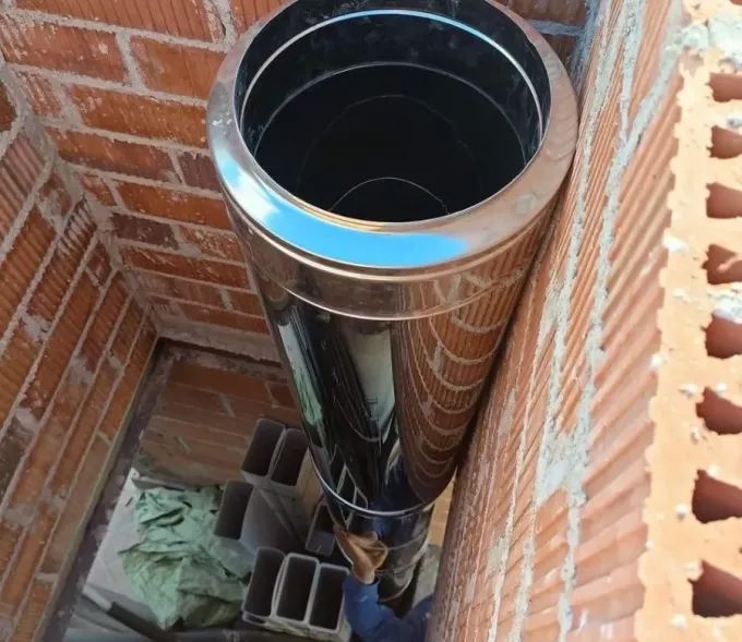 Instalación de un tubo metálico de doble pared en posición vertical dentro de un conducto de mampostería de ladrillo rojo.