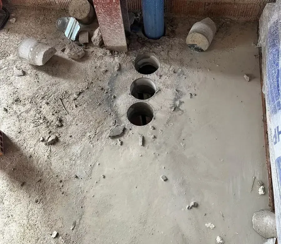 Una superficie de suelo de hormigón con tres agujeros circulares perforados en línea recta junto a una tubería azul.