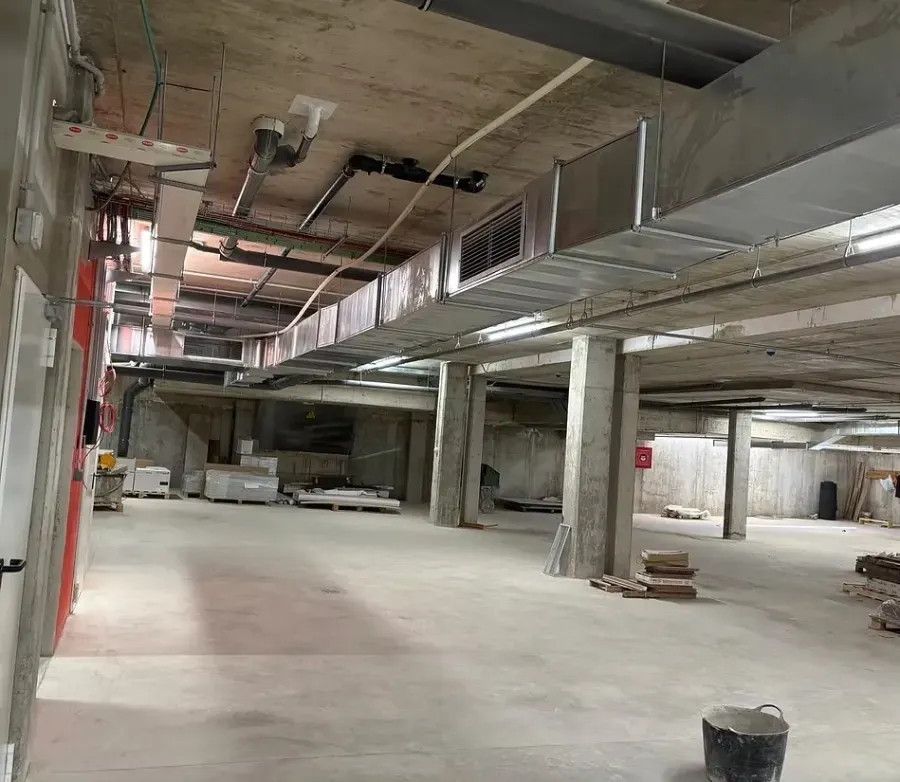 Local comercial sin terminar con techo de hormigón visto, conductos de ventilación y pilares estructurales a la vista.