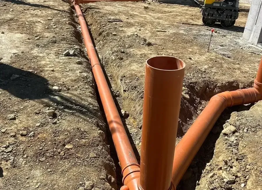 Tuberías de alcantarillado de color naranja tendidas en una zanja de tierra abierta en una obra en construcción.