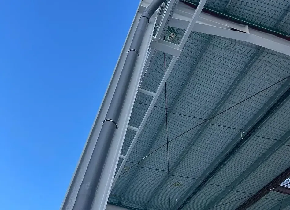Vista desde un ángulo bajo de una viga de acero gris que sostiene una cubierta metálica bajo un cielo azul brillante.