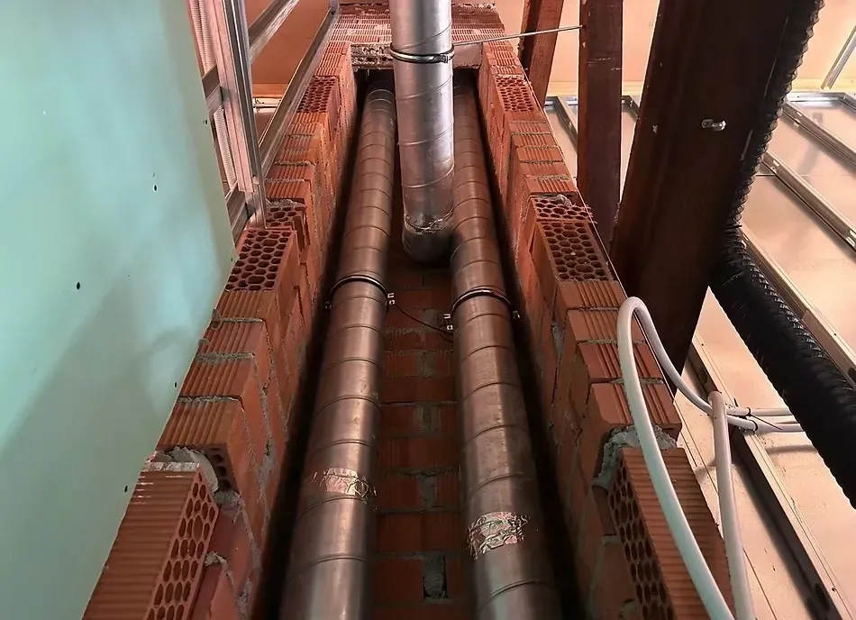 Dos tuberías verticales de ventilación metálicas alojadas en el interior de un estrecho conducto.