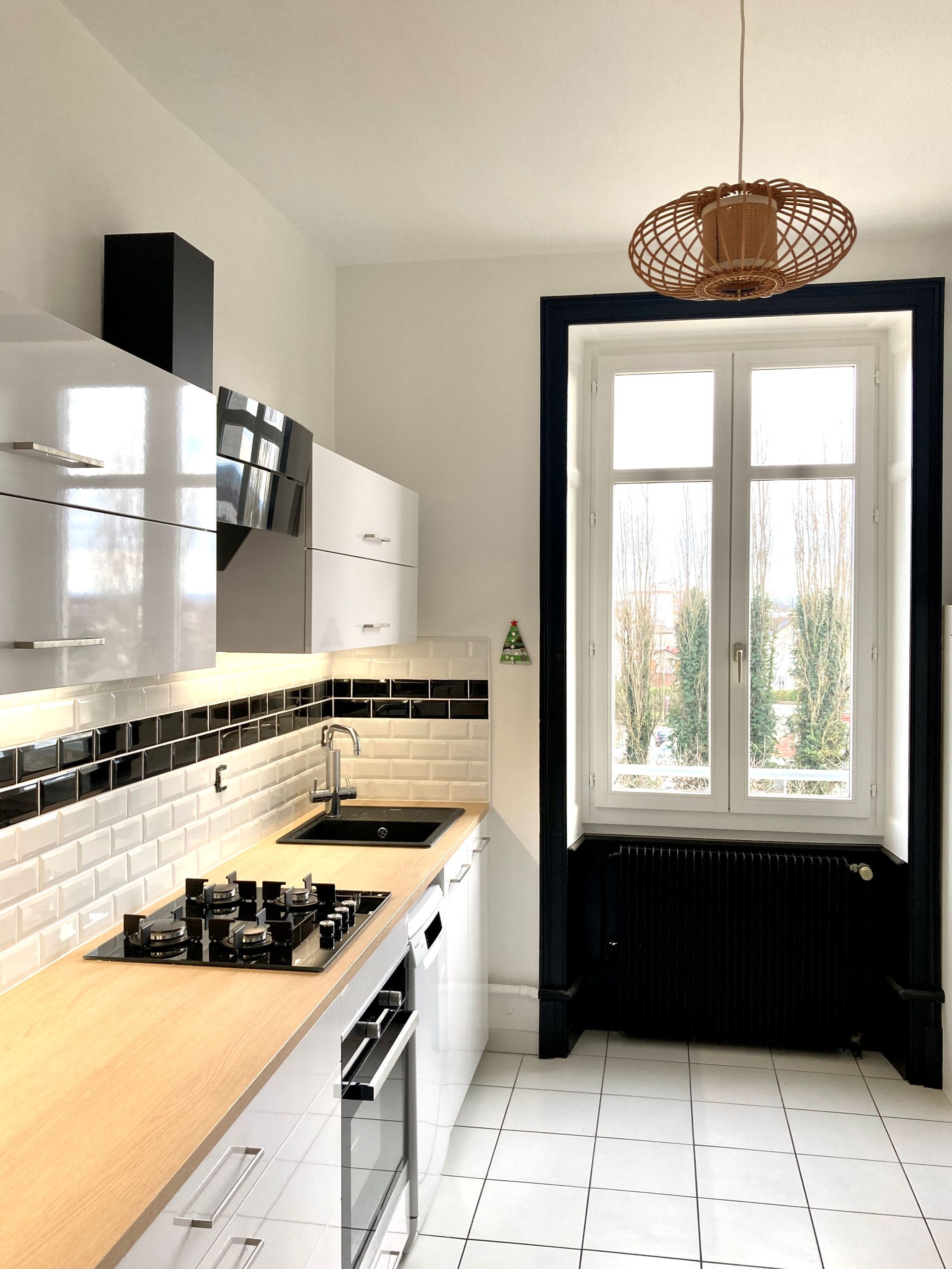 Cuisine moderne avec placards blancs, plan de travail en bois, crédence noire et une grande fenêtre.