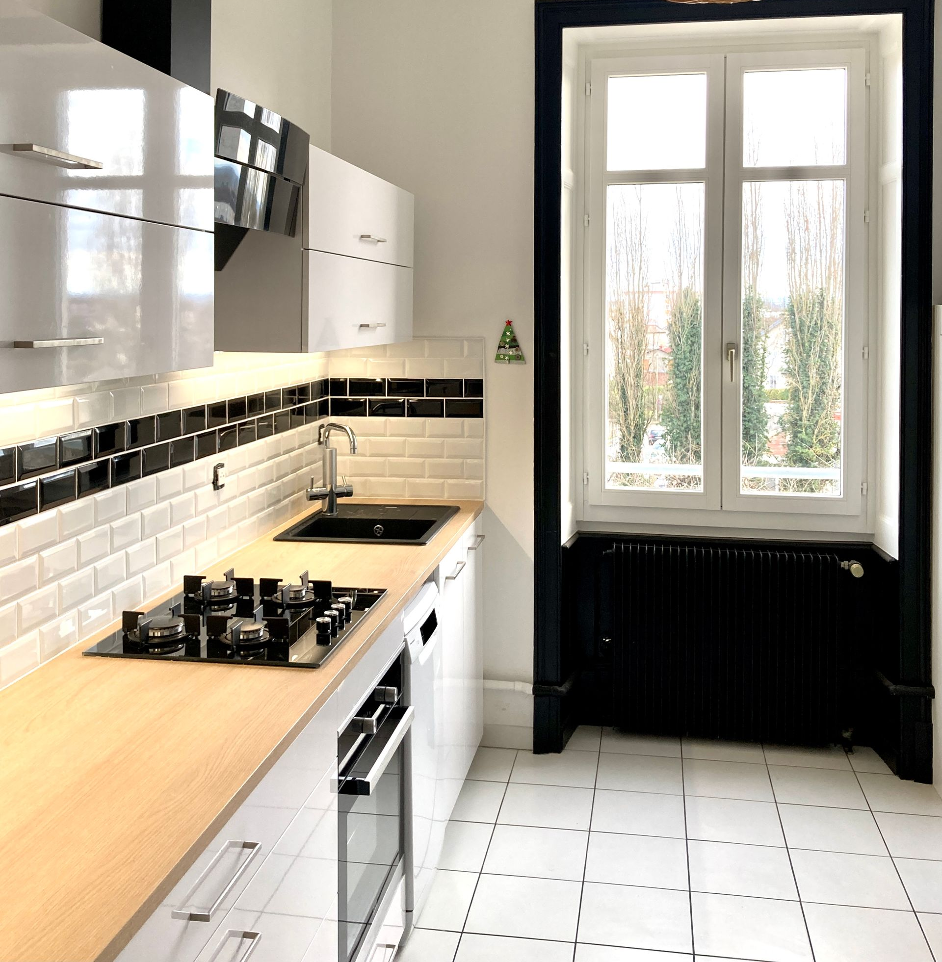 Cuisine moderne avec armoires blanches, comptoir en bois, touches de noir et fenêtre.