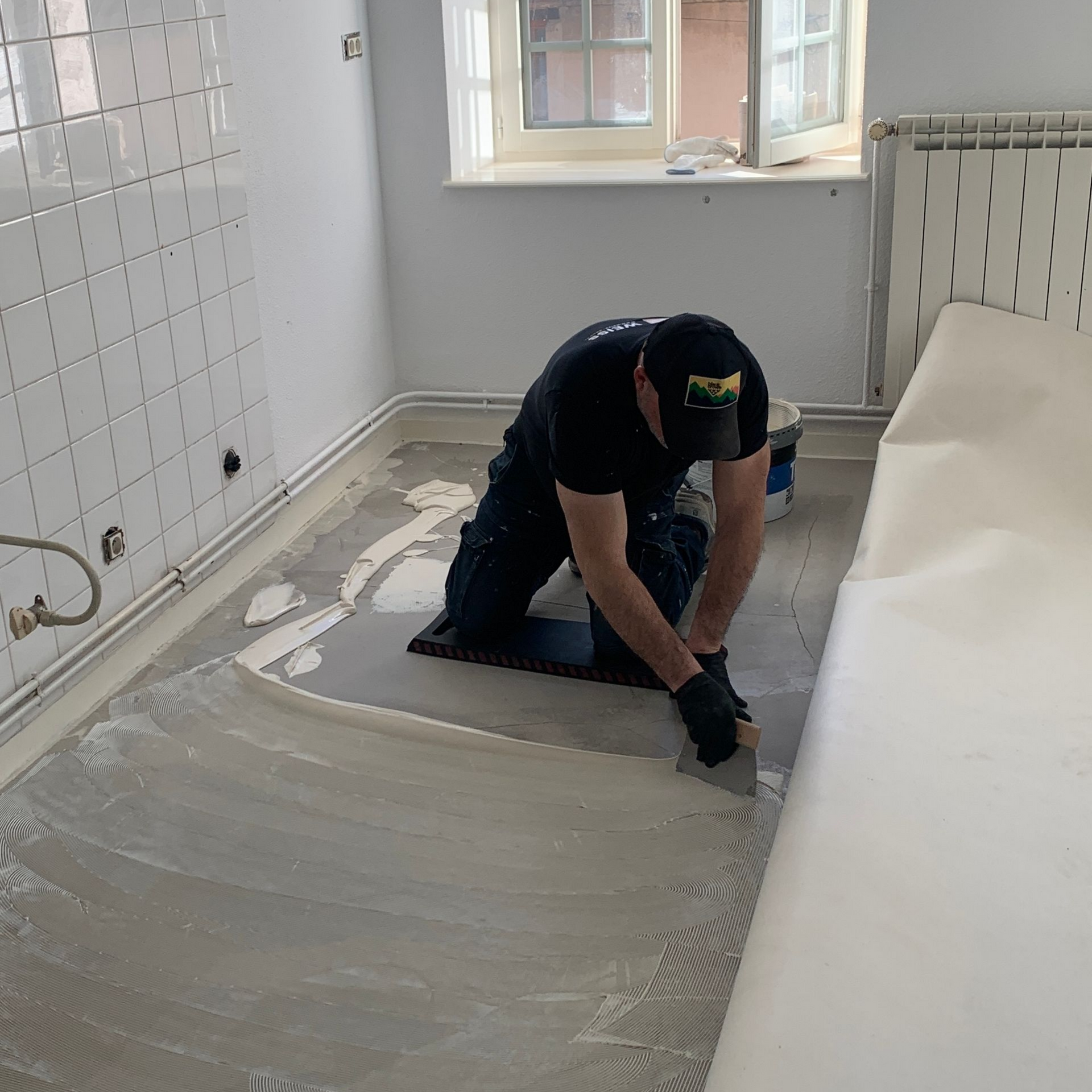 Un homme agenouillé applique de la colle sur le sol d'une pièce.