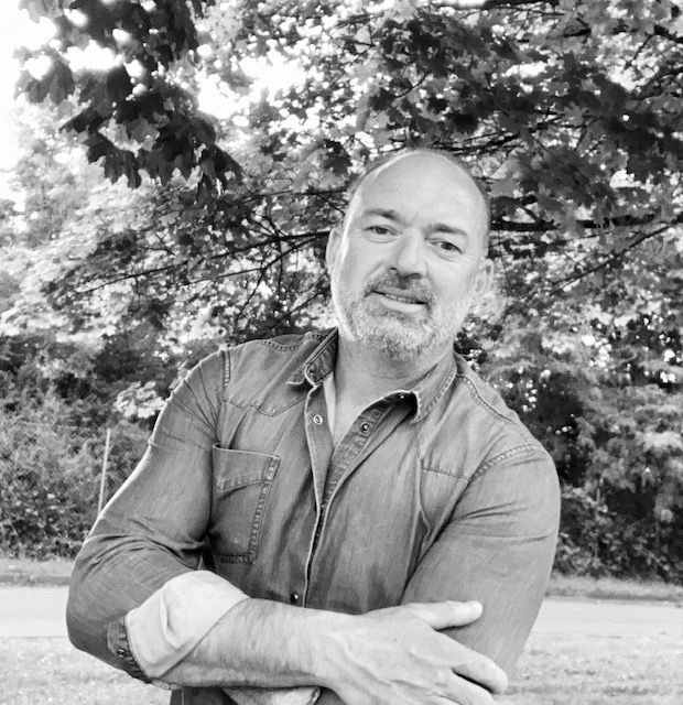 Homme les bras croisés, souriant, portant une chemise.