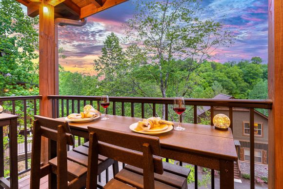 A wooden table with two plates of food and two glasses of wine on a balcony.