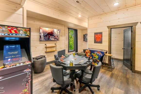 A game room with a table , chairs , and two arcade games.