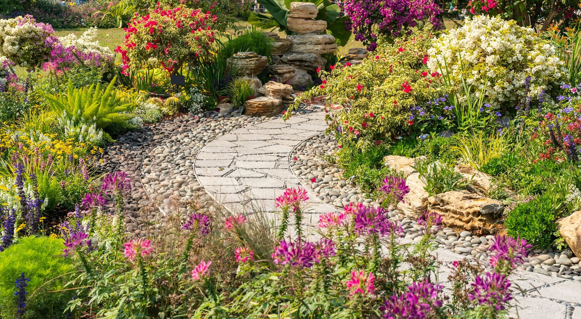 Allée de jardin en pierre serpentant entre des fleurs colorées et une végétation luxuriante