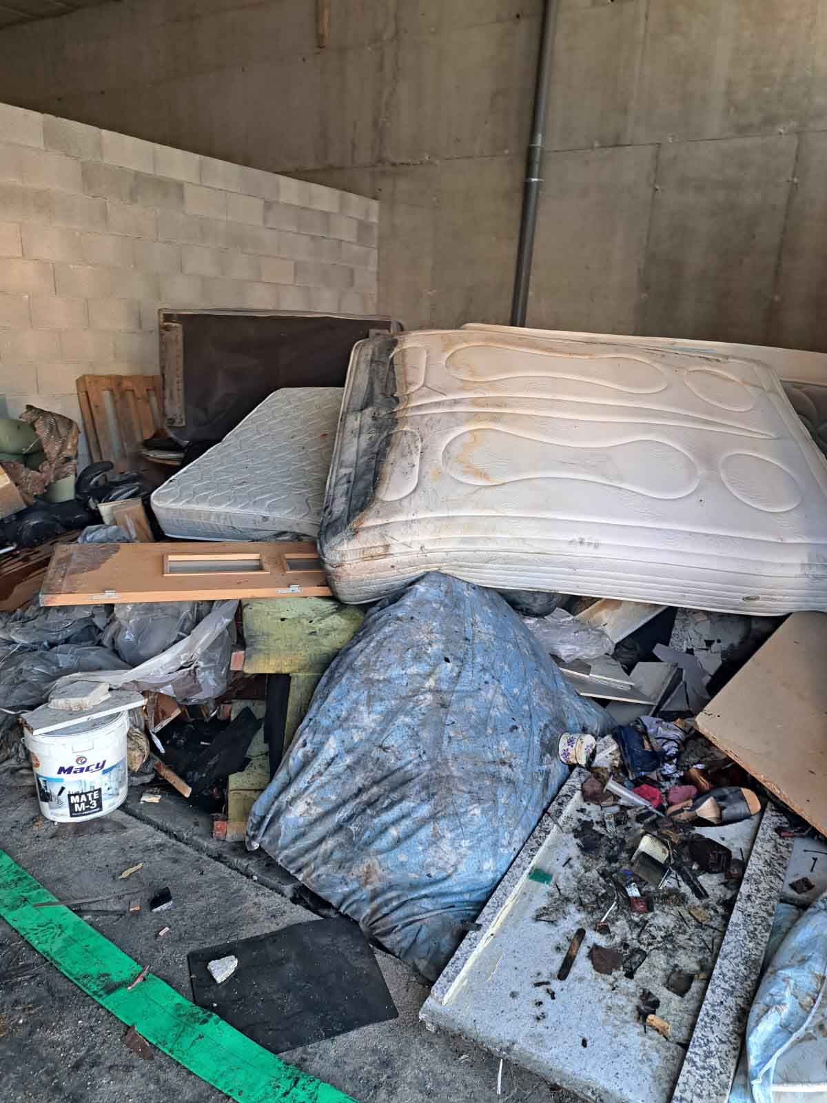 Un montón de basura en un garaje con un colchón encima.
