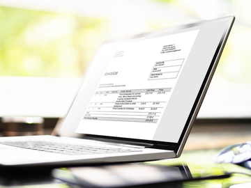 Ordinateur portable ouvert affichant une facture sur un bureau avec un arrière-plan lumineux flou.