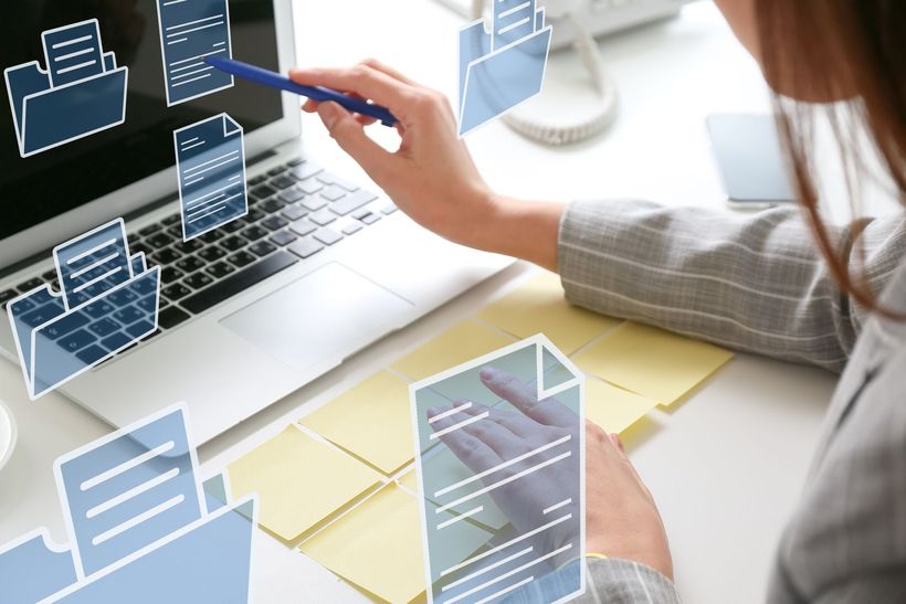 Une personne utilisant un ordinateur portable avec des icônes de documents numériques flottantes au-dessus du clavier.