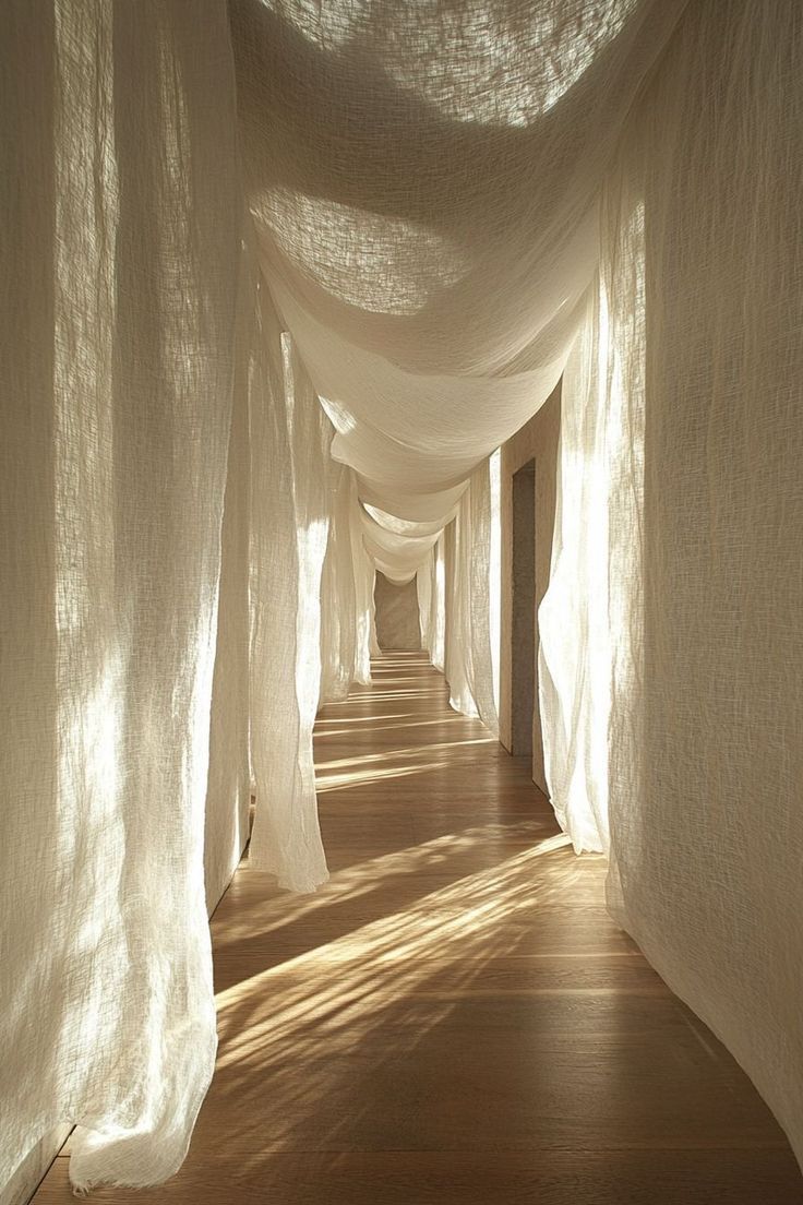Largo pasillo cubierto con tela blanca transparente, iluminado por la luz del sol.