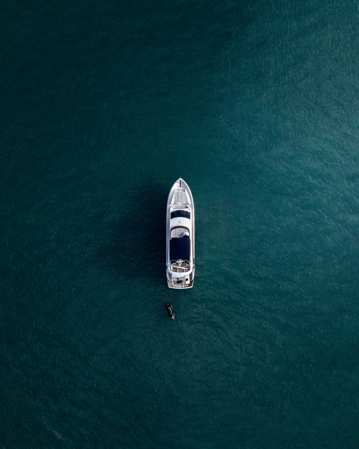 Un barco flota en aguas turquesas oscuras. Una persona nada cerca de la embarcación.