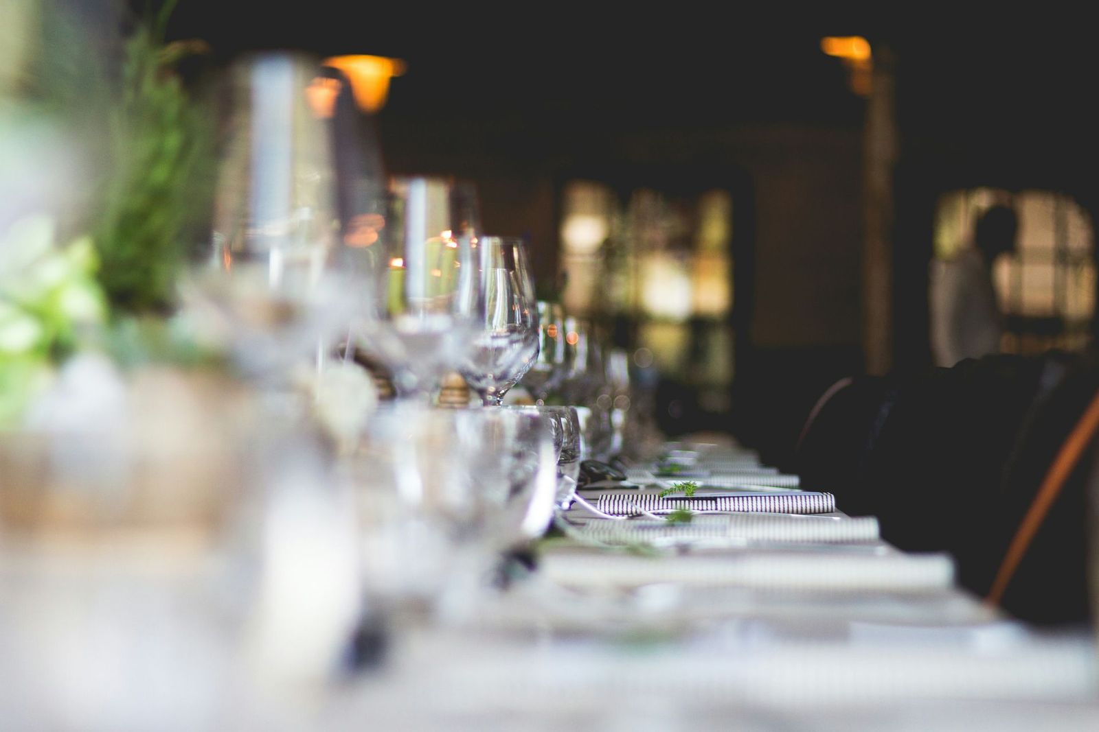 Mesa larga dispuesta para una cena formal, con copas de vino, platos y sillas oscuras en un restaurante.