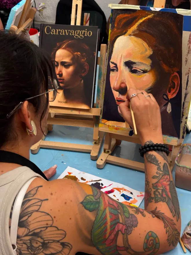 Persona pintando un retrato en una clase de arte, trabajando sobre un lienzo con el rostro de una mujer.