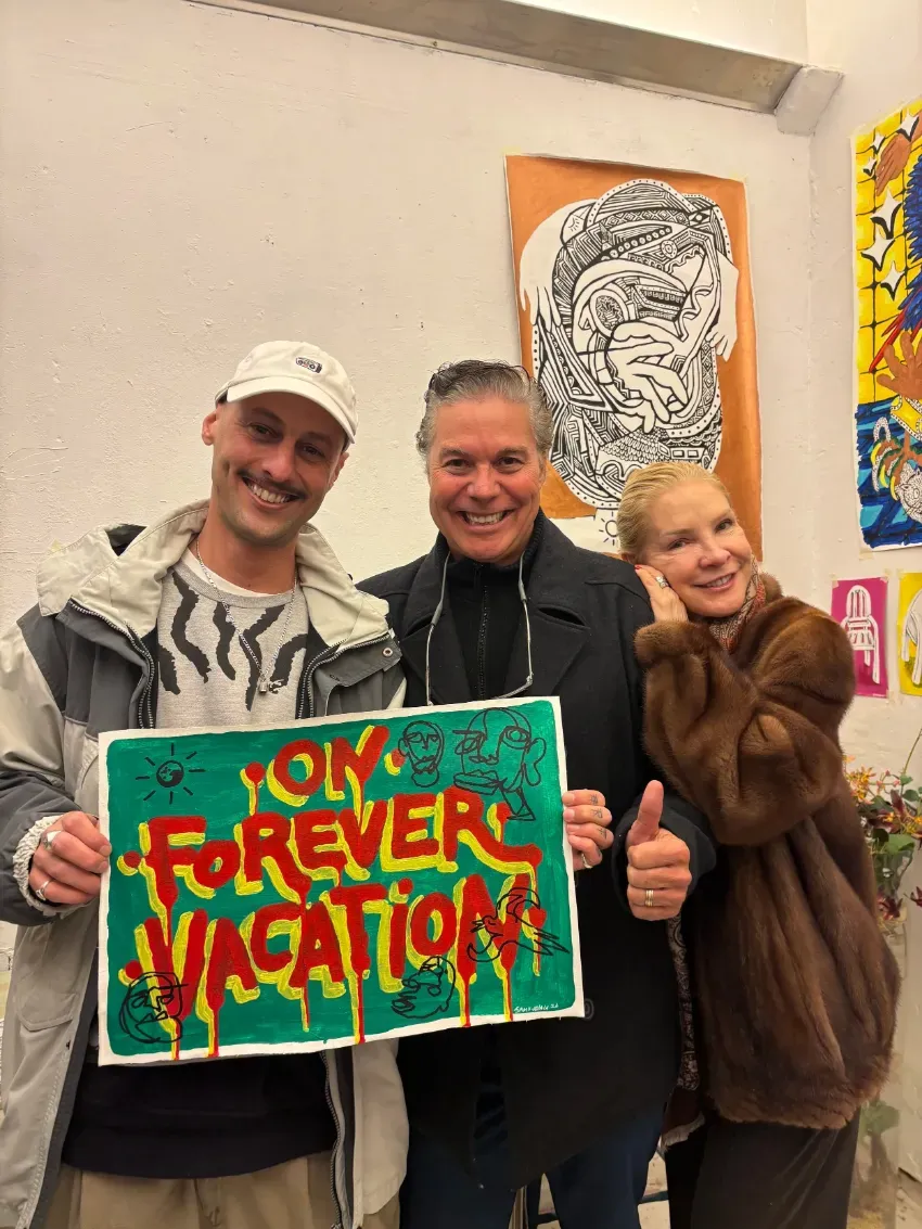 Tres personas sonriendo en el interior de un edificio, sosteniendo un colorido cartel que dice