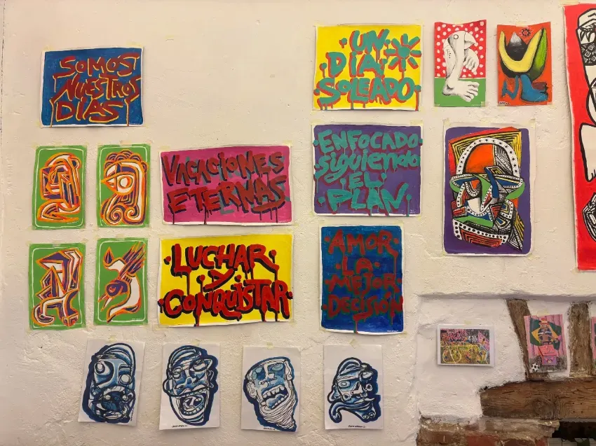 Obras de arte y máscaras coloridas pintadas a mano, dispuestas en una pared y un estante a modo de galería.