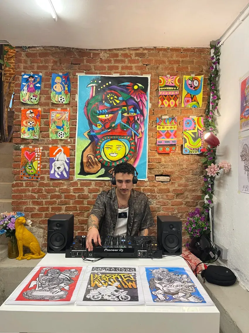 Artista en una mesa donde exhibe coloridas láminas y carteles en un estudio con paredes de ladrillo.