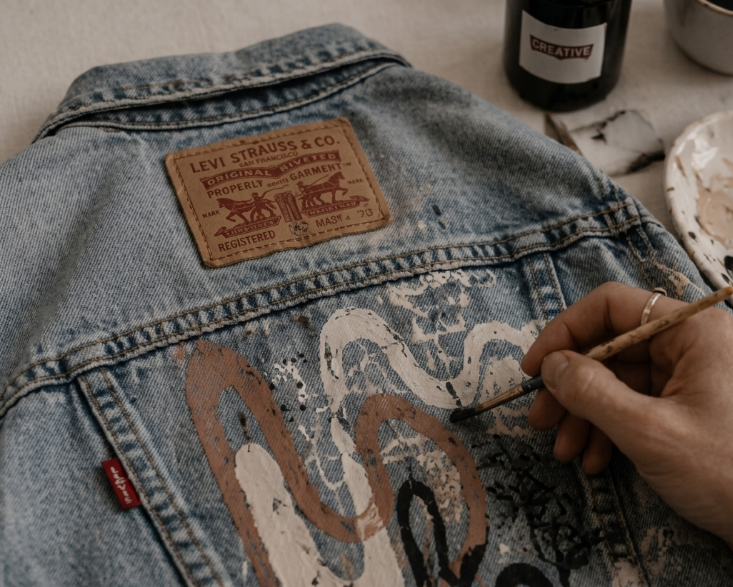 Diseños pintados a mano sobre una chaqueta vaquera azul claro con etiqueta Levi's y materiales de pintura a mano.
