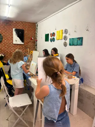Personas trabajando en escritorios blancos en un luminoso estudio de arte con cuadros en las paredes.