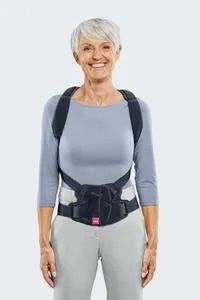 Mujer sonriente con un corsé negro y tirantes sobre un conjunto gris sobre un fondo blanco.