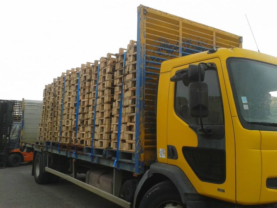 Camion à la cabine jaune transportant des palettes en bois.