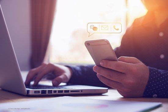 Person am Laptop mit Handy in der Hand