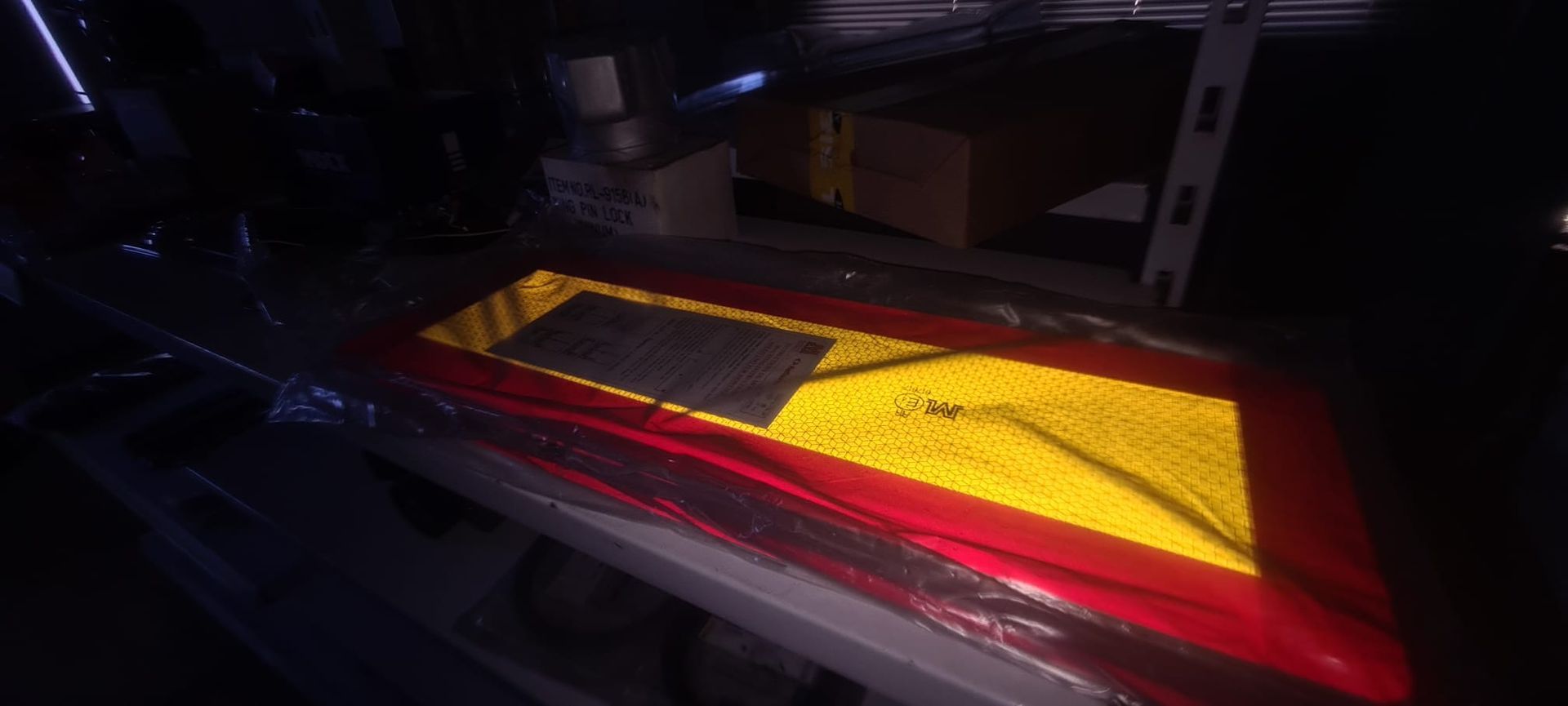 Un cartel rojo y amarillo está sobre un estante en una habitación oscura.