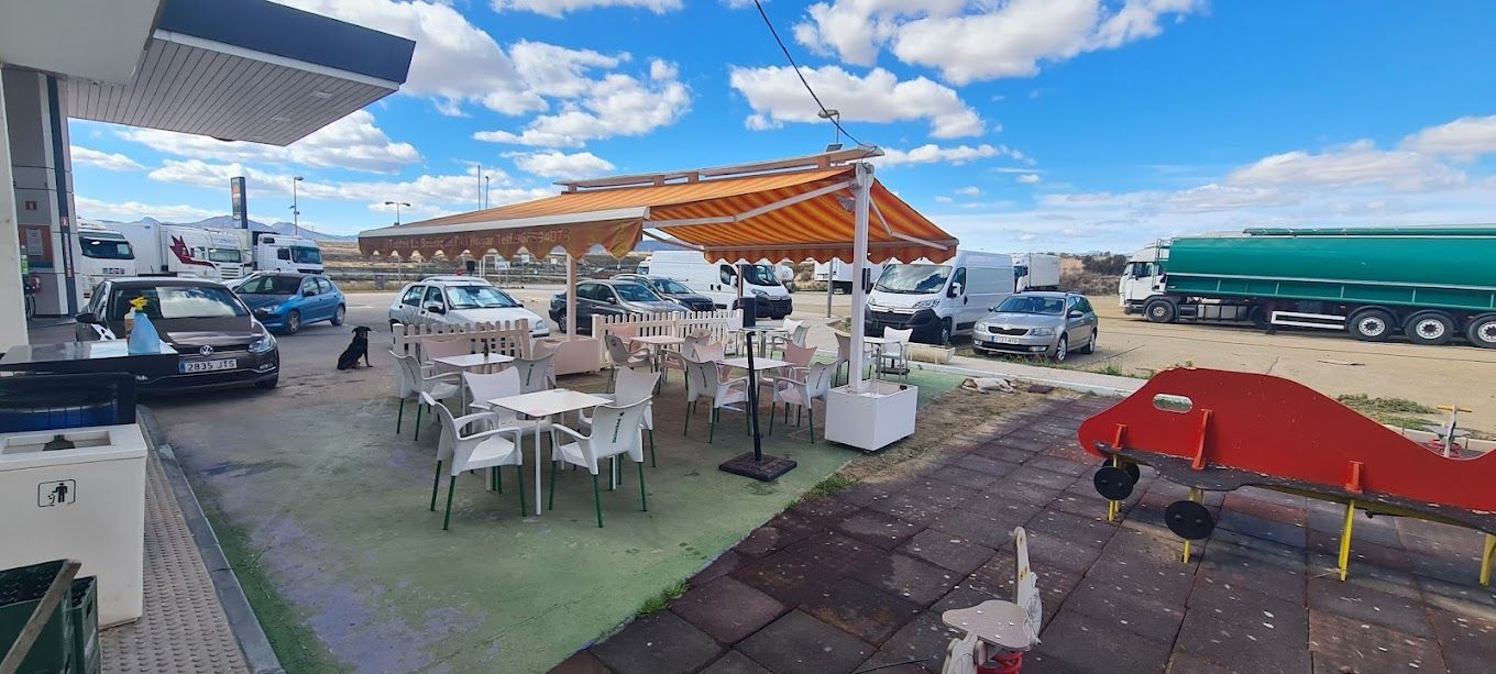Una gasolinera con mesas y sillas y un camión al fondo.