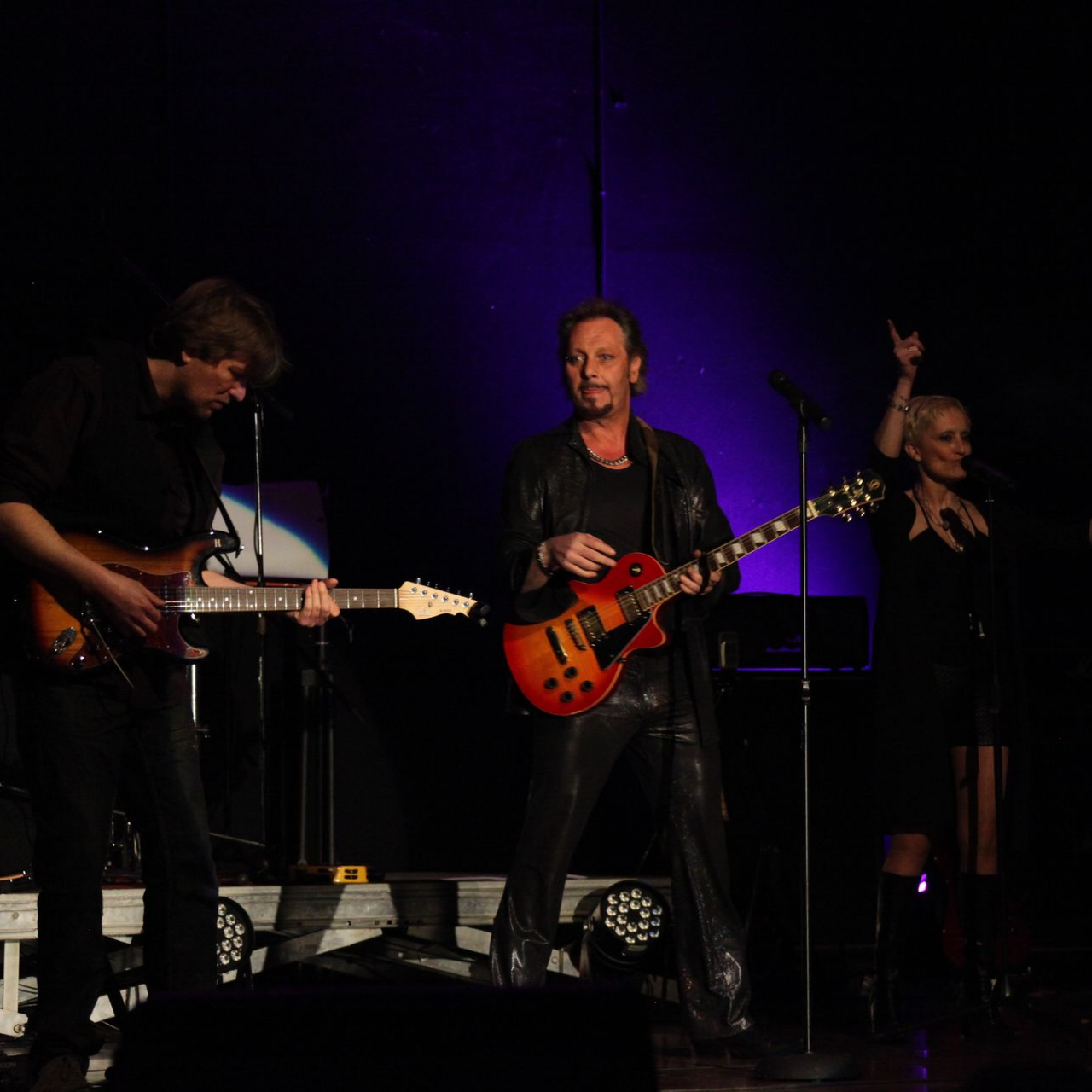 Un groupe joue en studio. Un guitariste et trois femmes et un JOHNNY DEMS chantent au micro.
