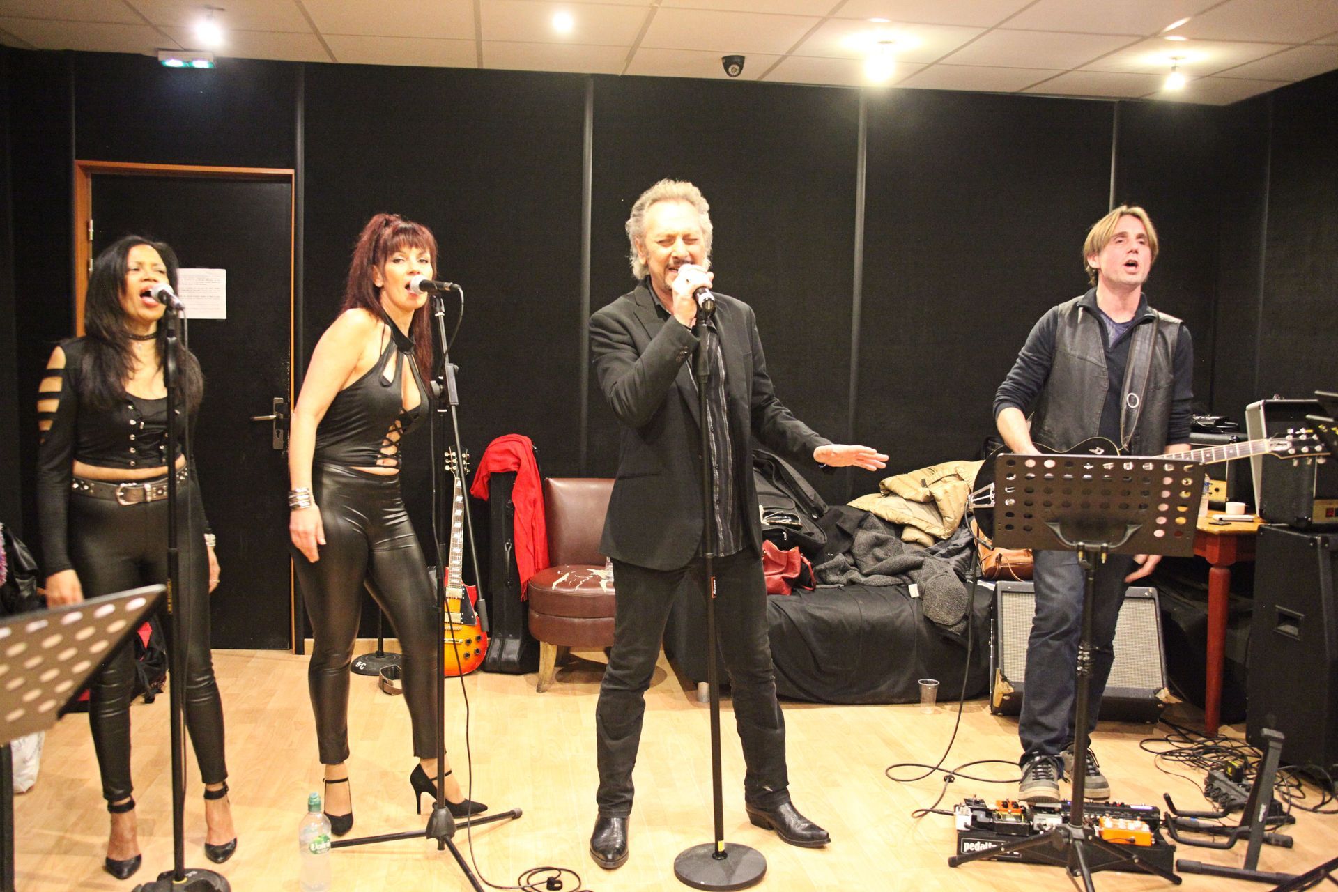 Un groupe joue en studio. Un guitariste et trois femmes et un JOHNNY DEMS chantent au micro.