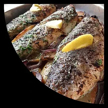 Un primer plano de una sartén de pescado con rodajas de limón encima.