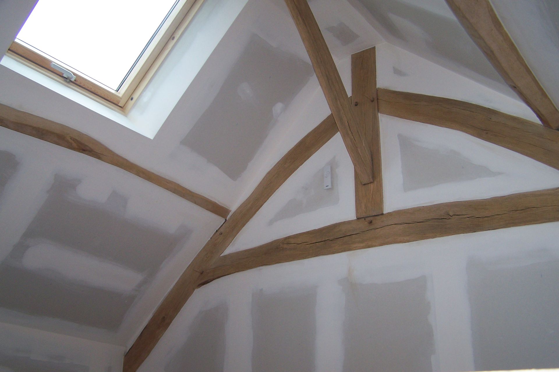 Intérieur en plaques de plâtre blanches avec poutres en bois apparentes ; un puits de lumière est visible.