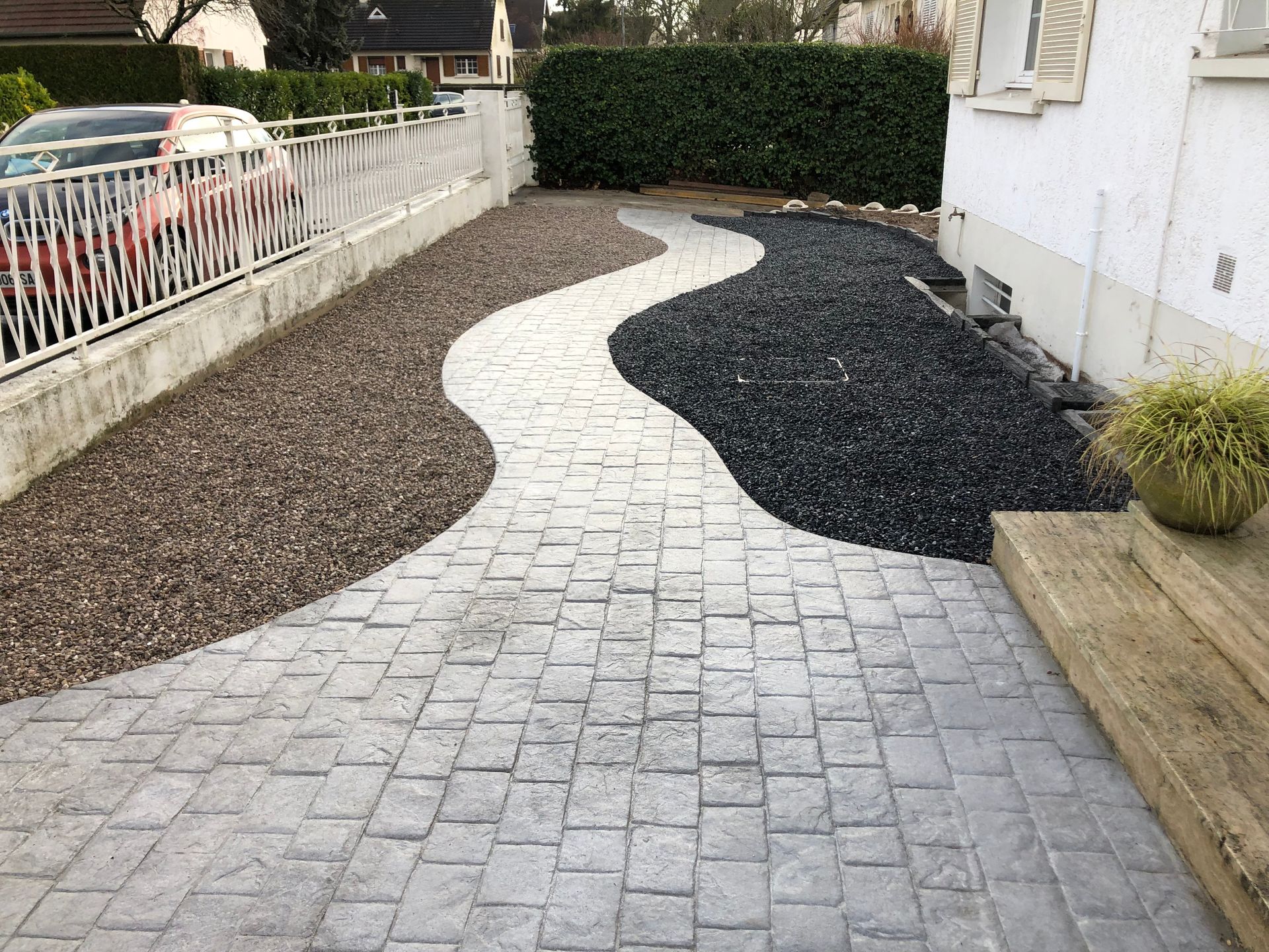 Un chemin pavé sinueux flanqué de gravier brun et noir, menant à une maison blanche.