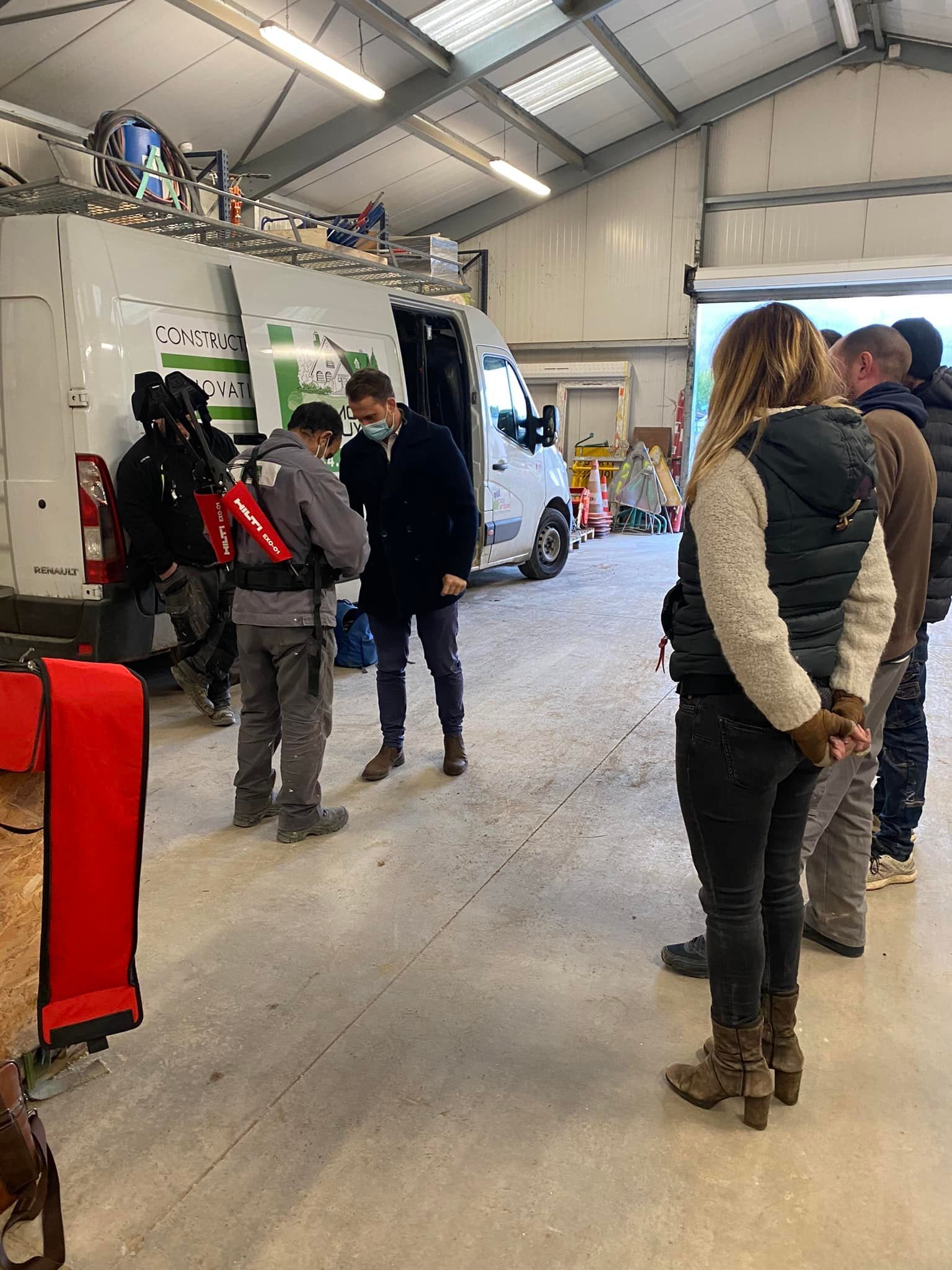 Des gens debout dans un atelier près de camionnettes, l'un d'eux portant un masque.